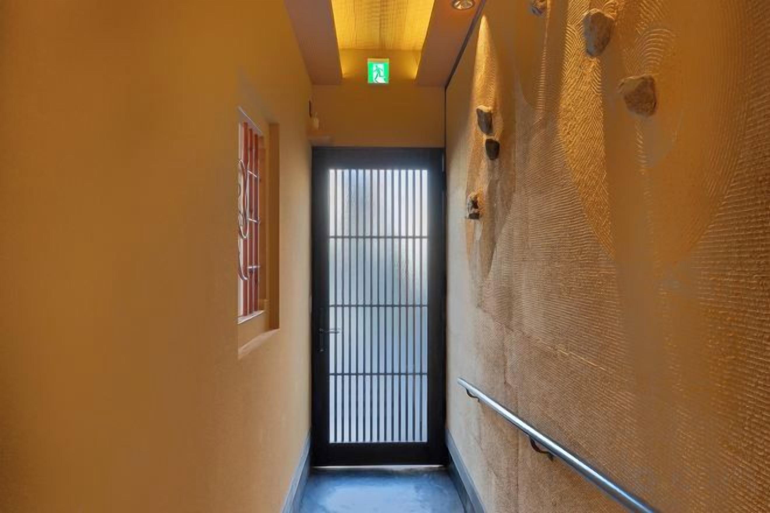 A narrow hallway with a door at the end, a handrail on the right, and a textured wall on the left.