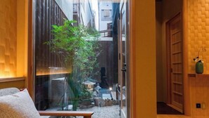 Un estrecho pasillo con un pequeño jardín, un banco de madera y una puerta de estilo japonés tradicional.