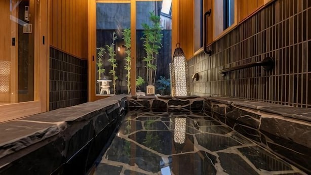 A traditional Japanese onsen with a stone bath, wooden walls, and a view of bamboo outside. - Kyoran Akaritei (Kyoto)