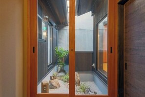 Un couloir étroit aux murs en bois et un petit espace jardin agrémenté de rochers et de plantes.