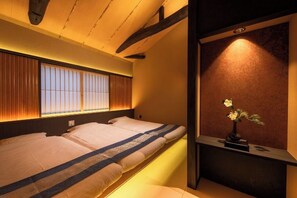 A room with two beds, a window with blinds, a vase with flowers, and a wooden ceiling. - Kyoran Akaritei (Kyoto)