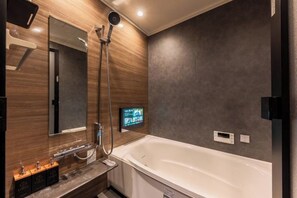 A modern bathroom with a large bathtub, a handheld showerhead, a wall-mounted TV, and a wooden vanity with a mirror. - Kyoran Akaritei (Kyoto)
