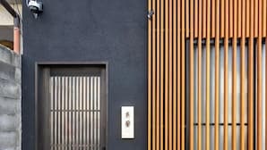 Fachada de un edificio con una puerta de color oscuro, diseño de paneles verticales de madera y un letrero con caracteres japoneses.