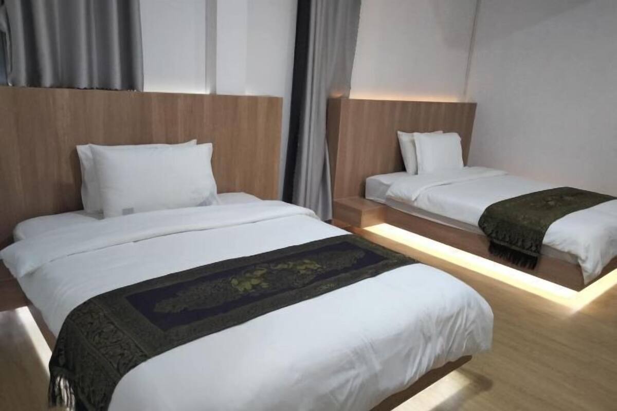 A hotel room with two beds, wooden headboards, and a large window with curtains.