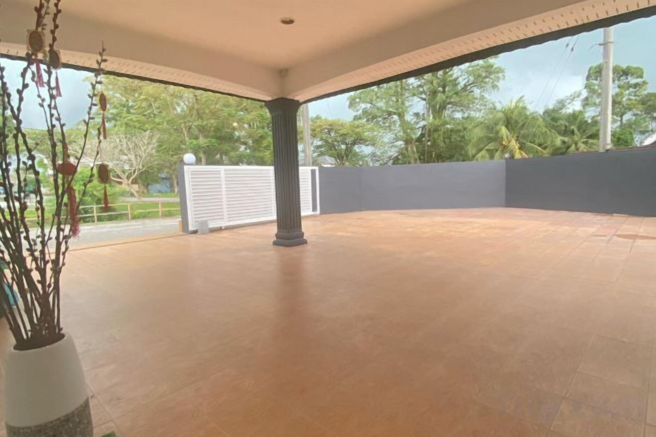An open terrace with a tiled floor, a potted plant, and a view of trees and a fence.