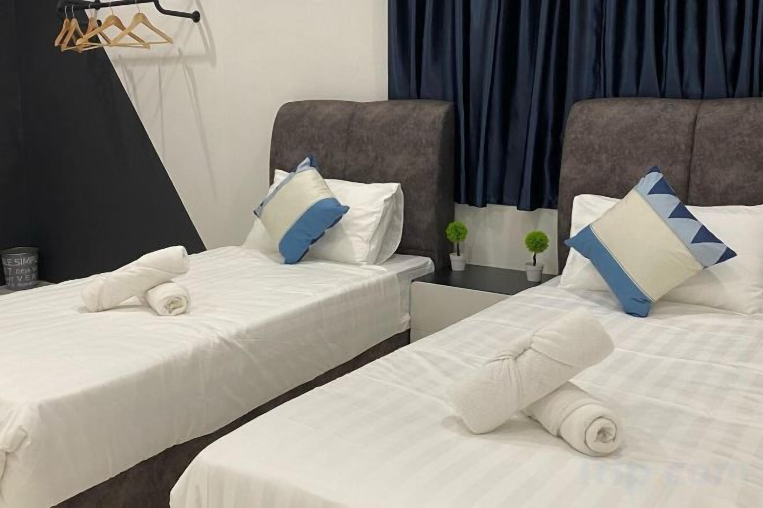 A hotel room with two beds, each with white linens and pillows, a small table with a plant, and a dark-colored headboard.