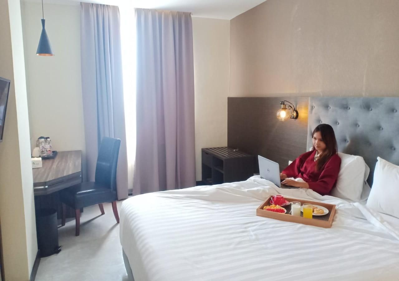 Habitación de hotel con cama, escritorio, silla, laptop y bandeja con alimentos para el desayuno.