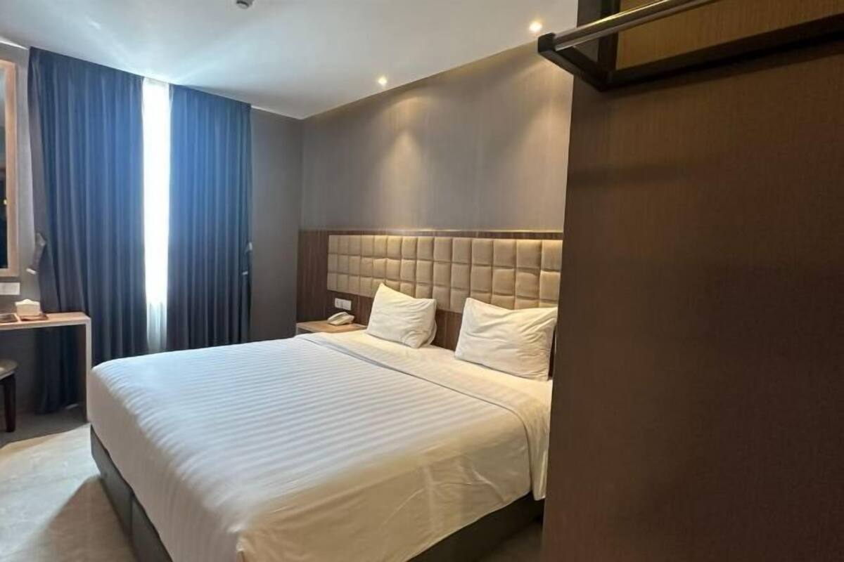 Une chambre d’hôtel avec un grand lit, une table de chevet, une commode et une fenêtre avec des rideaux.
