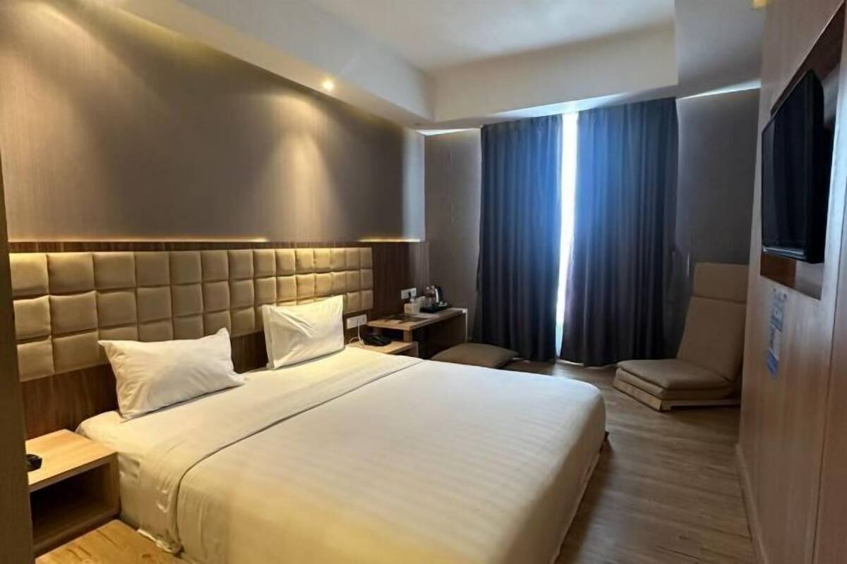 Une chambre d’hôtel avec un grand lit, une table de chevet, une chaise et une vue sur l’extérieur par une fenêtre.