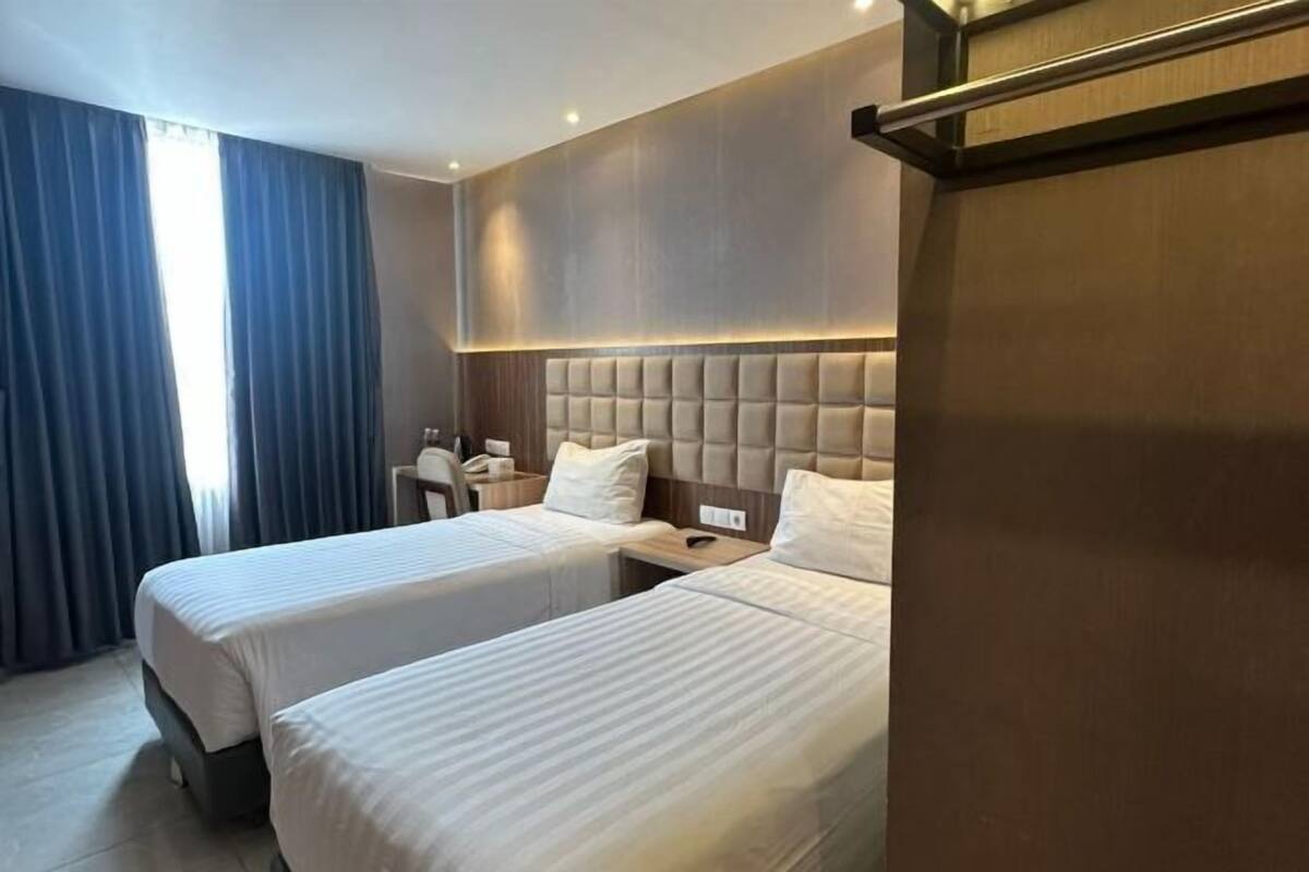 Une chambre d’hôtel avec deux lits, une table de chevet, une chaise et une grande fenêtre avec des rideaux.