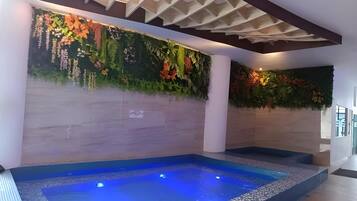 Een wellnessruimte met een bubbelbad, een wand met hangplanten en een plafond met houten details.