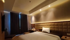 A hotel room with a large bed, a bedside table, a chair, a desk, and a TV. - OPA Hotel Palembang (Palembang)