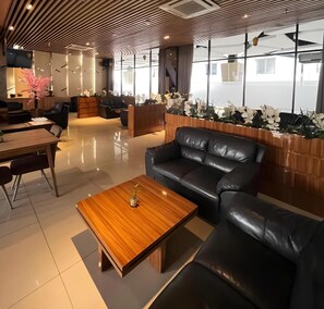 A modern interior with a leather sofa, wooden coffee table, and a reception desk with white flowers.