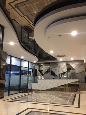 A modern interior with a curved ceiling, a central staircase, and a reception desk. - Opa Hotel Palembang (Palembang)