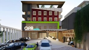 Un hotel moderno con un letrero llamativo, varios espacios de estacionamiento y una diversidad de vehículos.