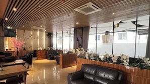 A modern hotel lobby with a wooden ceiling, a black leather sofa, a wooden reception desk, and a large window with a view of the city. - OPA Hotel Palembang (Palembang)