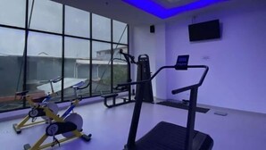 A gym with exercise equipment, large windows, and a ceiling with blue lighting. - OPA Hotel Palembang (Palembang)
