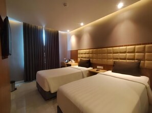 Ein Hotelzimmer mit zwei Betten, einem Holzkopfteil, einem Nachttisch mit Lampe und einem Fenster mit Vorhängen.