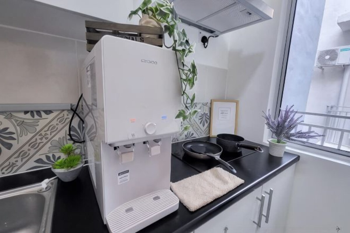 Una cocina con dispensador de agua, un lavamanos, una ventana con vistas y una planta en maceta.