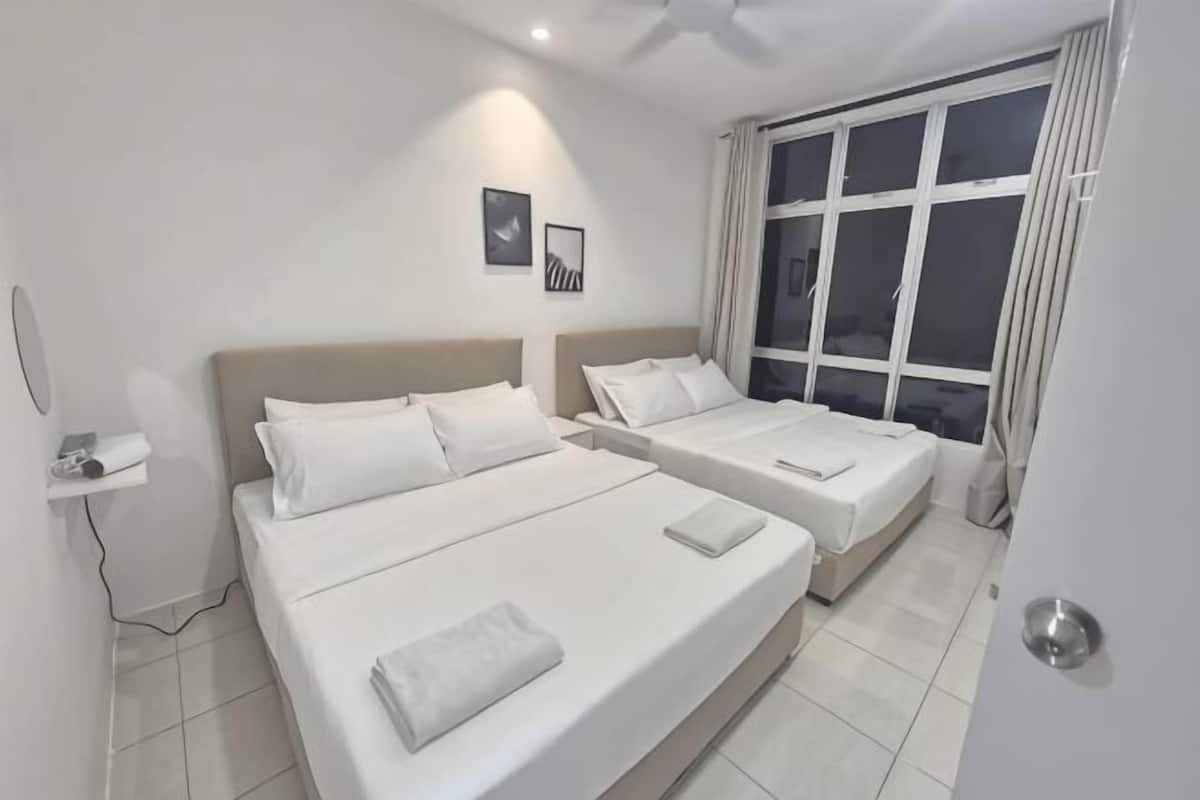 A hotel room with two beds, a window with curtains, a wall-mounted phone, and a small shelf.