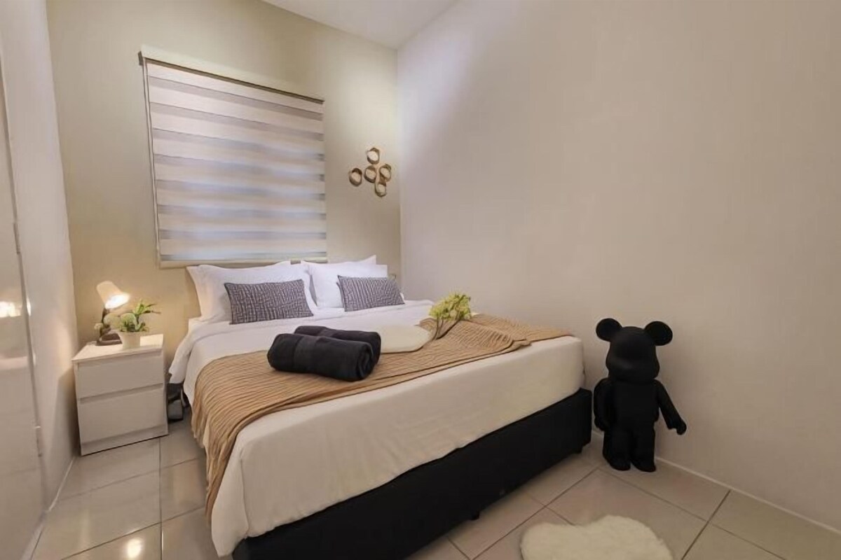 A neatly made bed with pillows and a blanket, a bedside table with a lamp, a teddy bear, and a wall-mounted light fixture.
