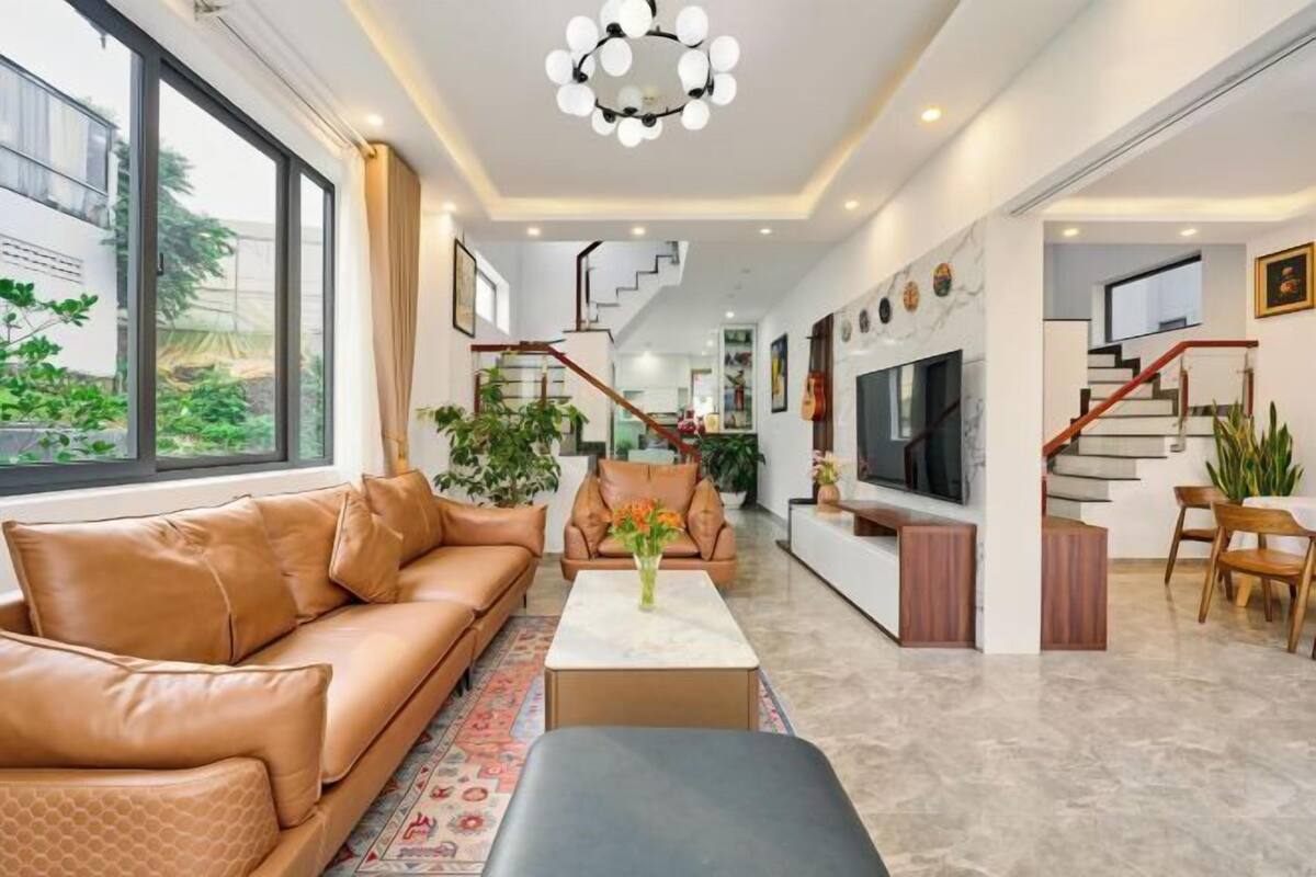 A modern living room with a leather sofa, a coffee table, and a TV. There is a staircase leading to another level.