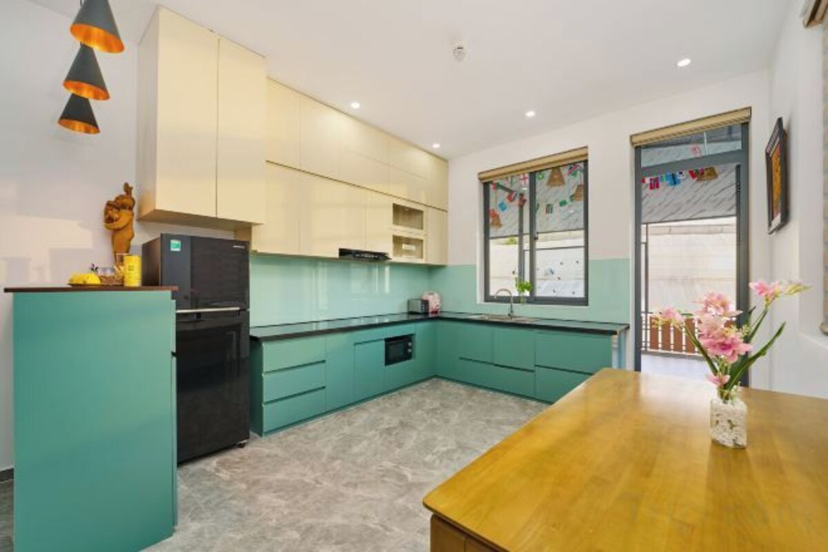 A kitchen with teal cabinetry, a wooden dining table, and a refrigerator.