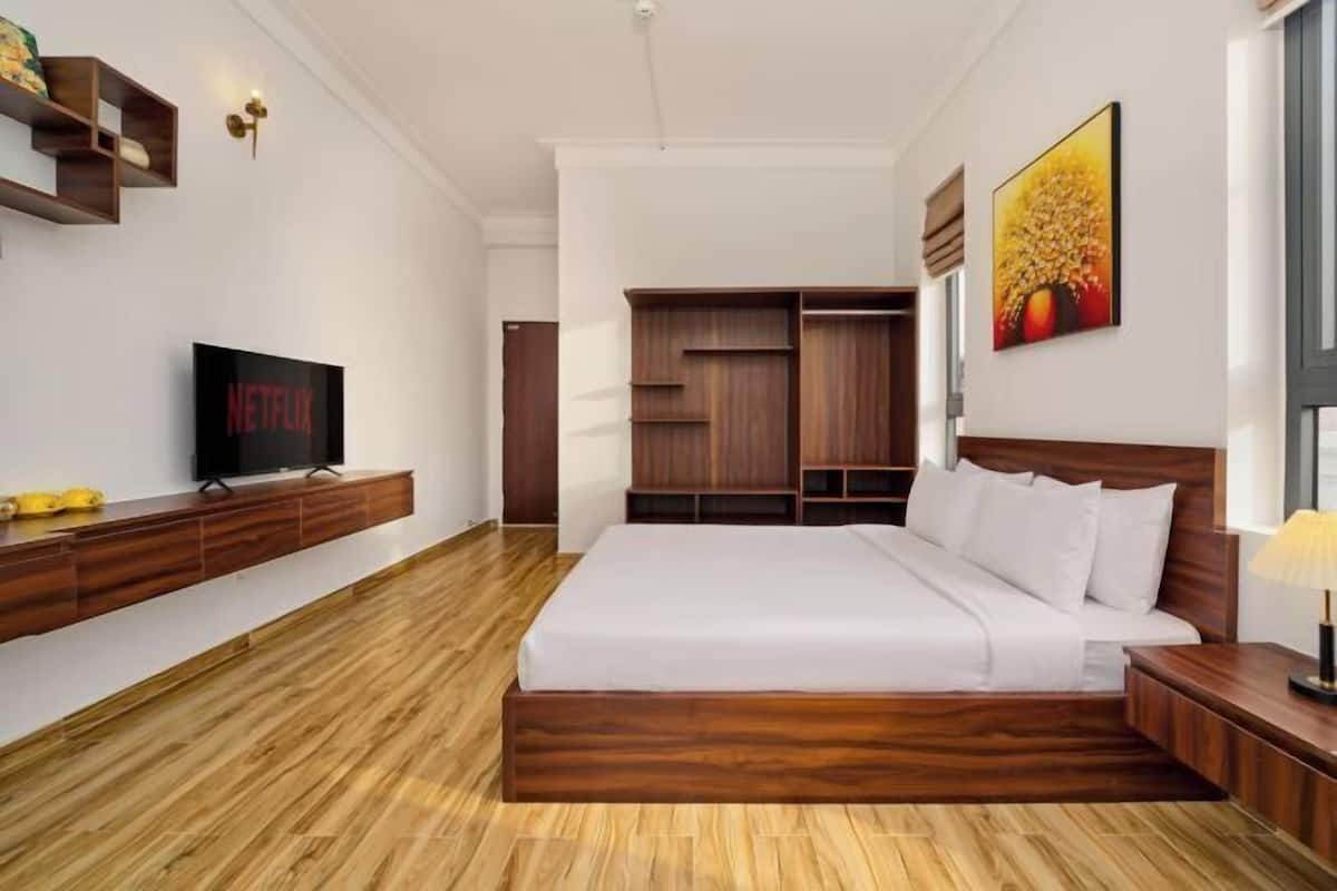 A modern bedroom with a wooden floor, a bed with white bedding, a TV on a wooden console, and built-in wardrobes.