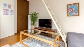 Un salon avec un téléviseur, une plante, une échelle et un tableau accroché au mur.