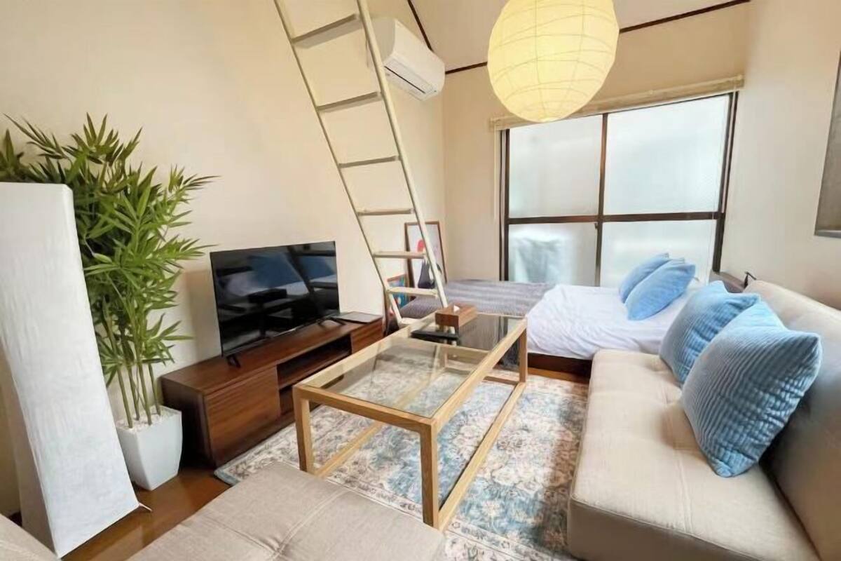 Una sala de estar moderna con un sofá, una mesa de centro de vidrio, un televisor, una escalera, un ventanal grande y una planta.