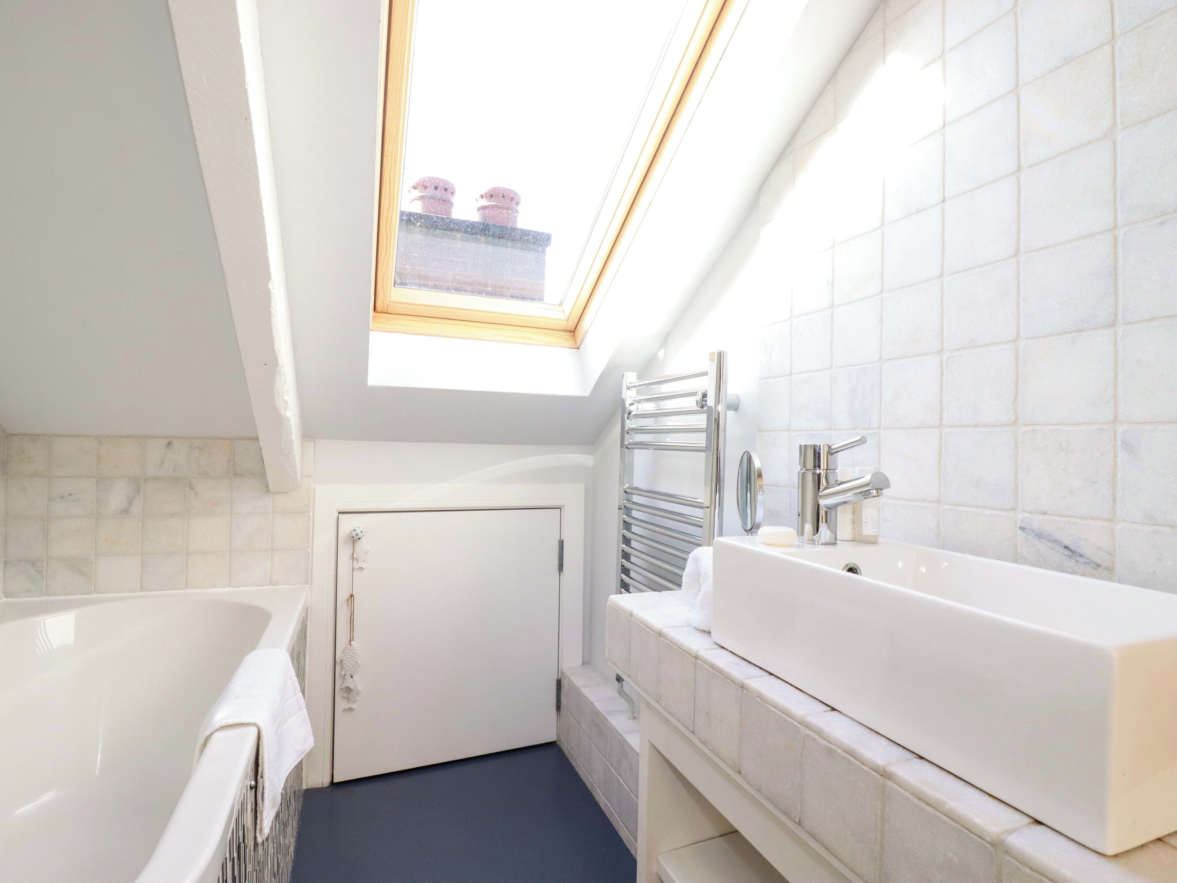 Une salle de bain moderne dotée d’une lucarne, d’une baignoire, d’un lavabo avec un miroir et d’un porte-serviettes.