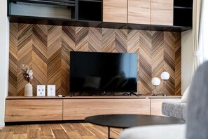 Uma sala de estar moderna com uma grande televisão de tela plana, parede de madeira em padrão herringbone, armários embutidos e uma mesa de centro redonda.
