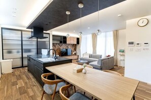 A modern kitchen with a central island, wooden flooring, and pendant lighting. - Mirai Stay KAWACHI (Kumamoto)