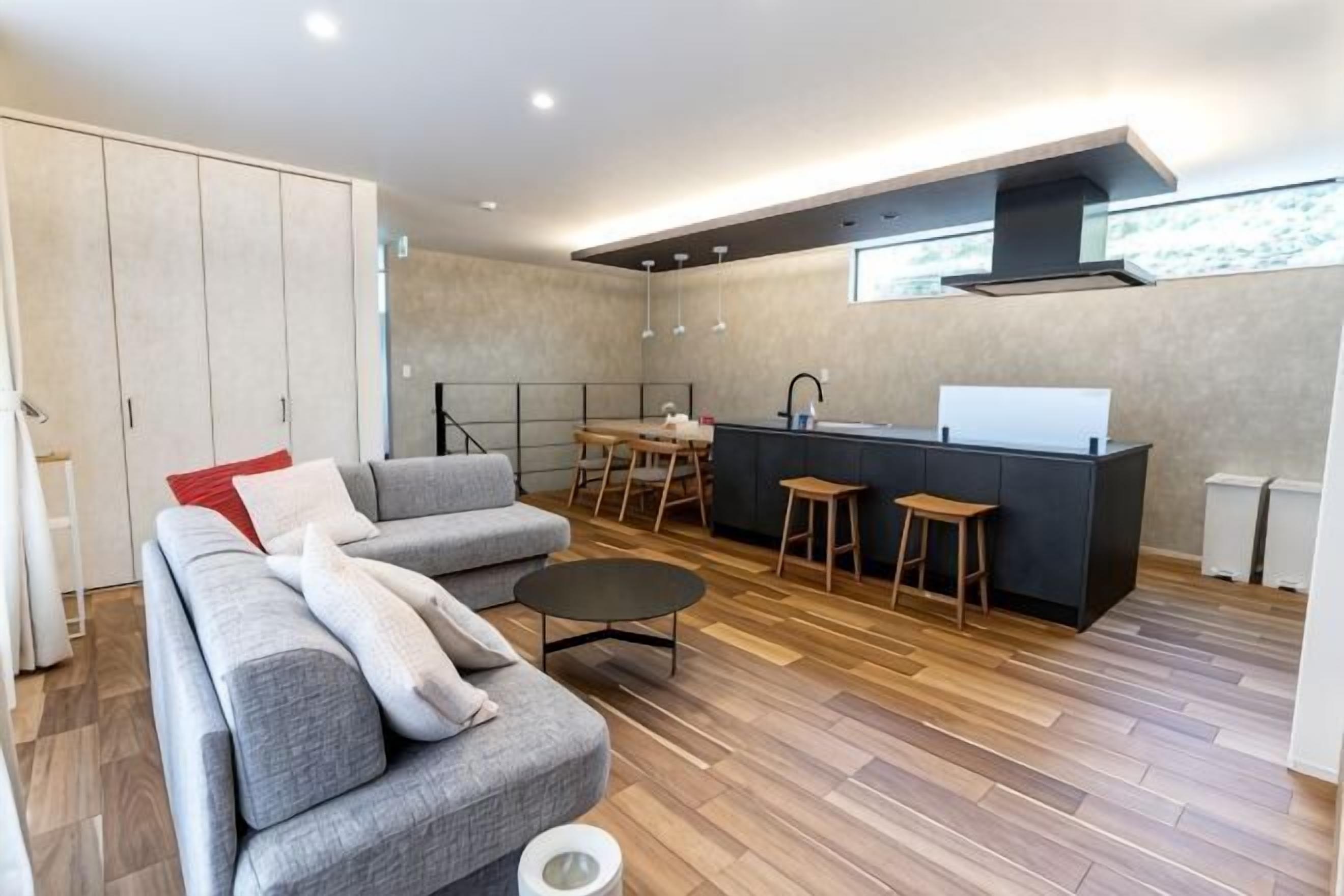 A modern living room with a sofa, a coffee table, and a kitchen area with stools and a counter.