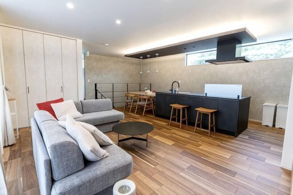 A modern living room with a sofa, a coffee table, and a kitchen area with stools and a counter.