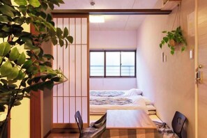 Ein kleines Zimmer mit Bett, Tisch und Meerblick durch ein Fenster.