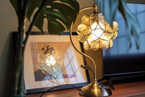 A desk lamp with a unique design, a framed picture on the wall, and a plant in the background. - Lumie (Tamatsukuri) (Osaka)