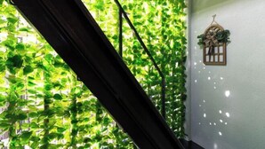 A room with a window covered by green foliage, a wooden slat, and a small hanging planter with plants. - Lumie （Tamatsukuri） (Osaka)