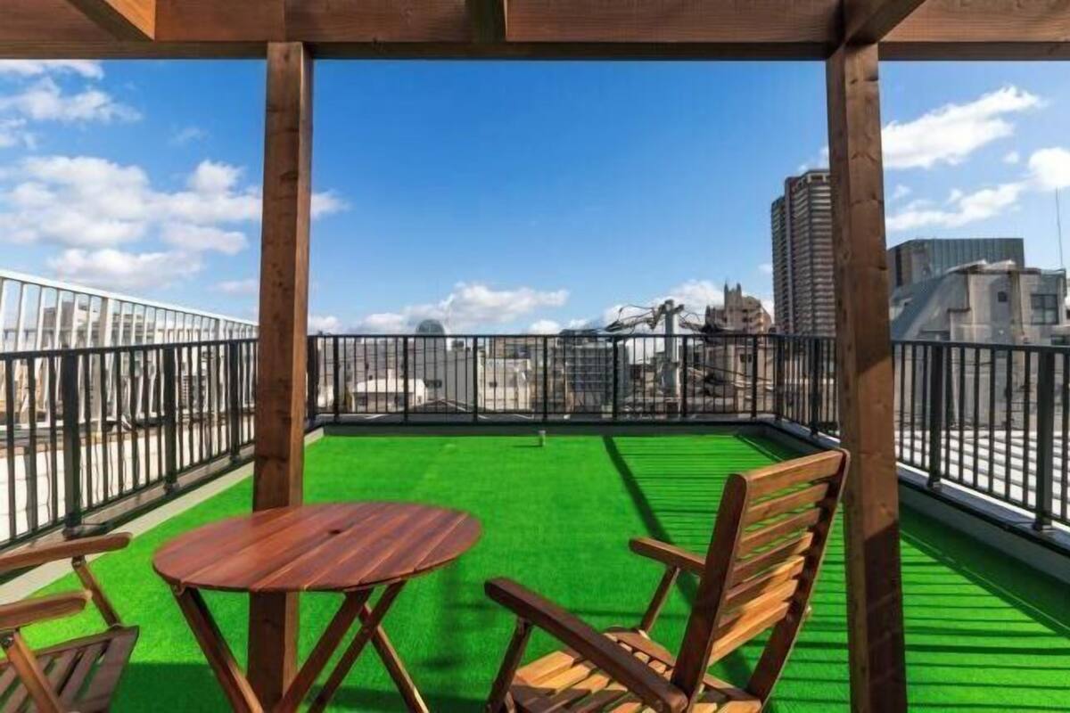 Un balcon agrémenté de gazon synthétique vert, de meubles en bois et offrant une vue sur les bâtiments de la ville.