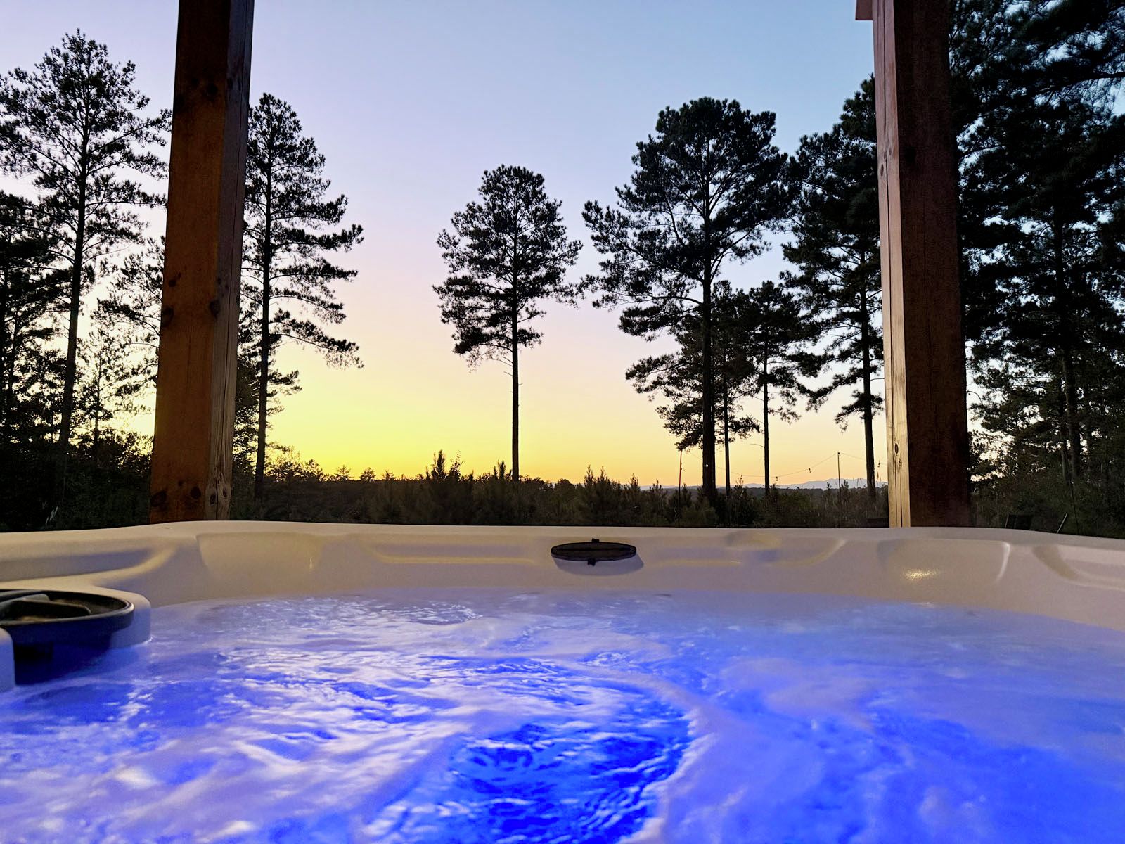 A hot tub with a view of tall trees and a sunset.