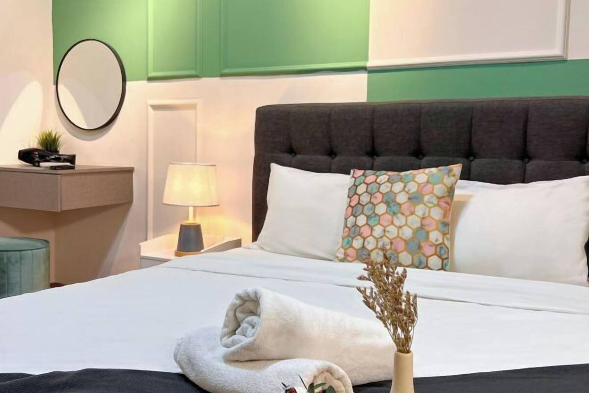 Une chambre d’hôtel avec un lit, une table de chevet avec une lampe, un miroir et un coussin décoratif.