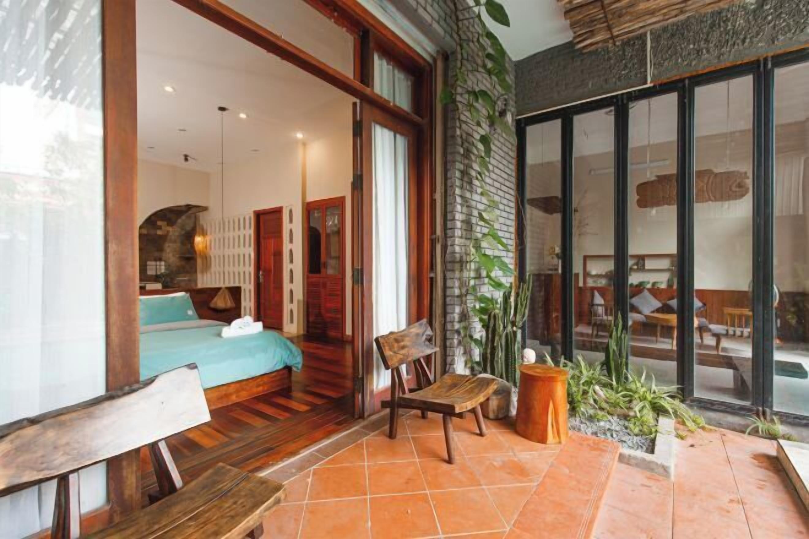 A room with a bed, a wooden chair, a small table, and a potted plant.