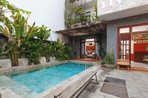 A swimming pool with a wooden deck, surrounded by lush greenery and a building with a modern design. - Chaca Beach (Da Nang Municipality)
