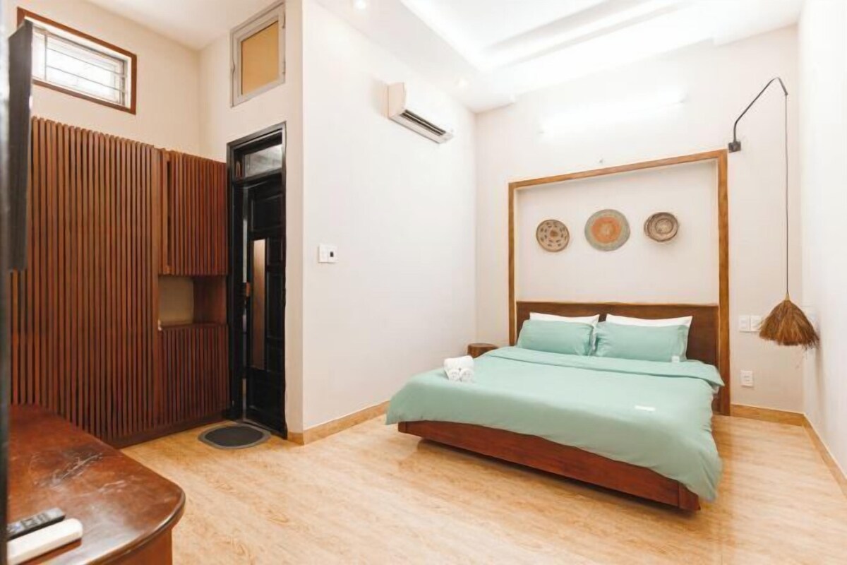 A bedroom with a bed, a wooden wardrobe, a desk, and a wall-mounted air conditioner.