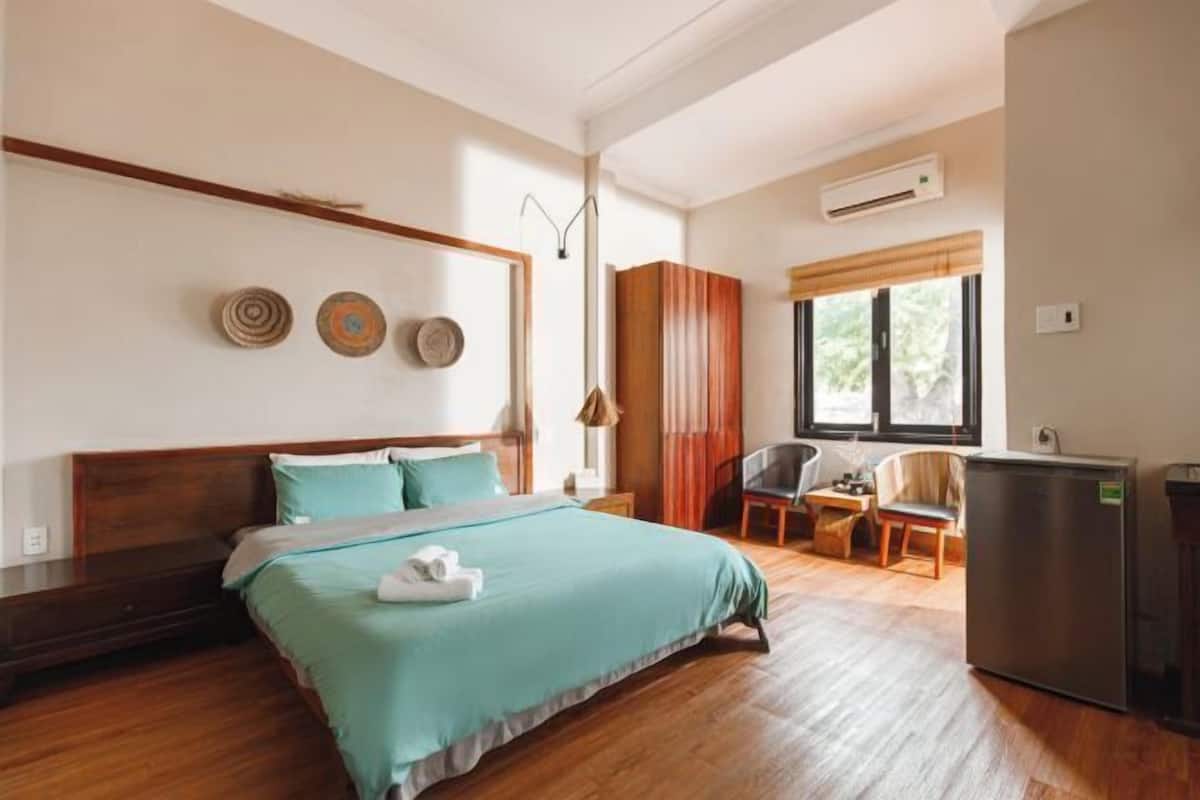 A hotel room with a bed, a desk, a chair, and a refrigerator.