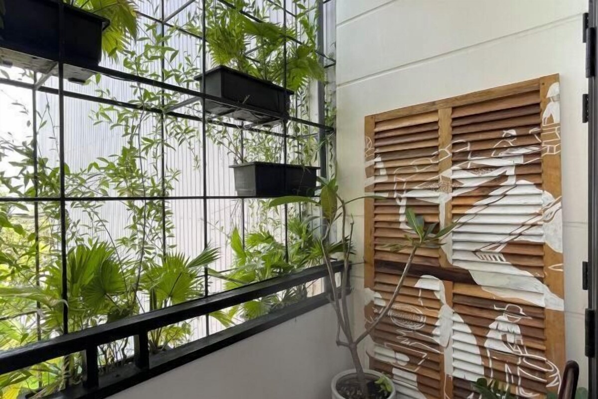 A room with a large window, a metal grid, and a wooden wall panel with a design.