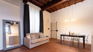 Un salon moderne comprenant un canapé, une table à manger avec des chaises, un grand miroir et un plafond avec des poutres apparentes.