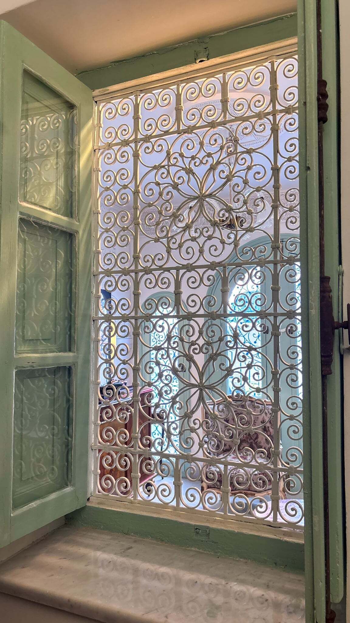 Une porte verte ornée de motifs métalliques complexes et une fenêtre avec des vitraux décoratifs.