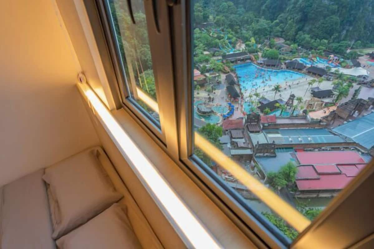 A room with a large window overlooking a resort area with multiple pools and tropical landscaping.