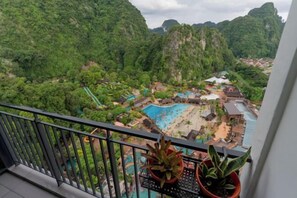 Un balcon agrémenté de plantes en pot, donnant sur un complexe hôtelier avec une piscine et des bâtiments nichés au cœur d’une végétation luxuriante.